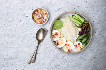 Healthy food brown rice dish with boiled eggs chili line has cucumber eggplant vegetable in bowl isolated on white slate table.