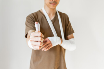 Young man with gauze bandage wrapped around his injured arms gesture thumb up. Man with hands wrapped in medical bandage on white background. First aid, treatment after accident injury. Copy space