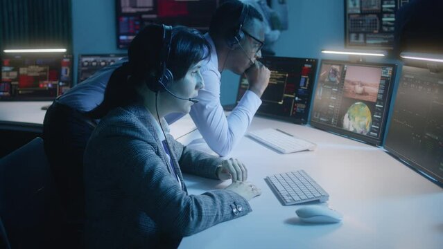 Female flight control operator with African American coworker monitor space mission on computer in command center. Team clap hands after successful space rocket launch displayed on big digital screens