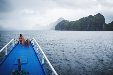 Couple sitting at the bow of the boat to relax and enjoy the misty landscape in El Nido, Philippines