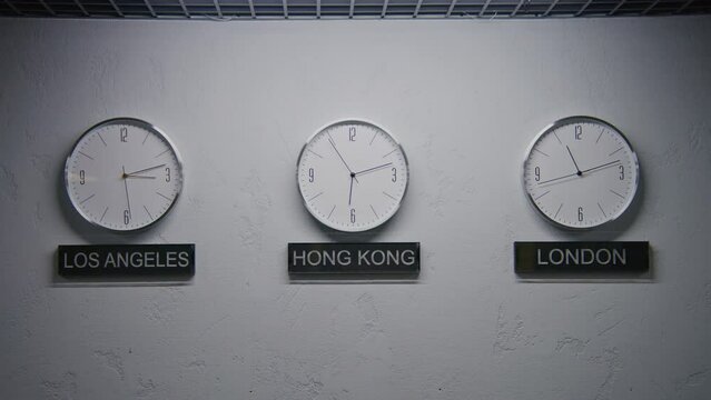 Walking wall clocks illuminated by LED lamp in office with modern design. Names of big cities written under clocks. Watches with running time pointers show time zones of different cities. Zoom in.