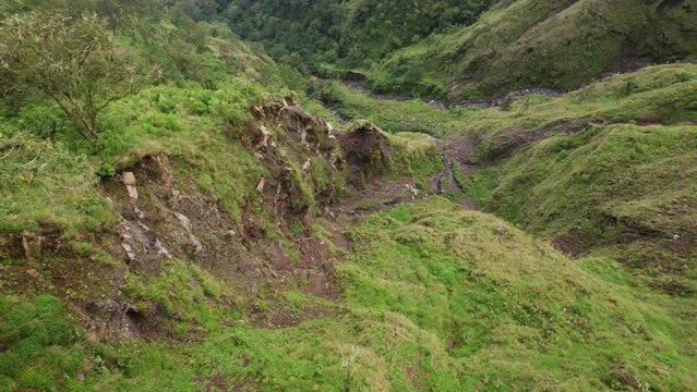 Rills on steep slope of Abang mountain, camera tilt down. Erosion reveal layers of soft soil and stones, traces of former geological activity. Unusual top-down perspective from height.