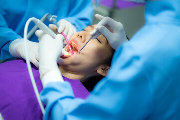 Fototapeta premium Dentist with an assistant in protective gloves are examining her teeth with a help of a dental bur with a mirror and an air polisher. Caries healing. Examination of the dentist.