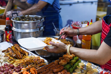 Vietnamese woman serving chicken paws in plastic box with chili in vietnamese night market