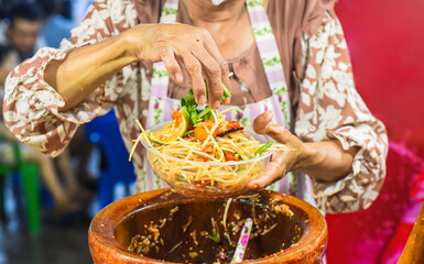 Vietnamese woman serving noodles with vegetables in vietnamese night market in food festival