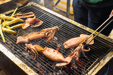 Many squids on a grill in vietnamese night market in food festival, process of cooking