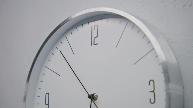 Static shot of walking wall clock in office with modern design. White watch with metal frame hangs on the wall and shows time. Strict design clock with running time pointer. Time interval. Close up.