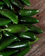 Green hot Jalapeno pepper. Lot of ripe peppers on wooden surface. Pepper harvest. Bright spices. Spicy food. Mexican pepper. Wooden background. Close-up. Soft focus. Top view. High quality photo