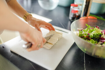 Womans hand cutting a feta cheese preparing healthy salad