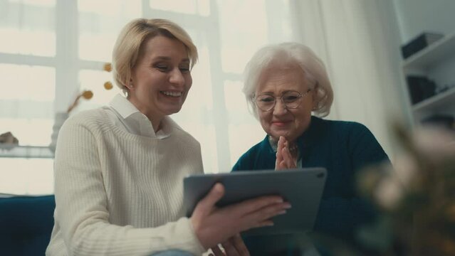 Senior mother, middle-aged daughter shopping online on tab, enjoying family time