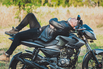 Fototapeta na wymiar Motorcyclist in jacket lying on his motorcycle in the countryside. Biker man lying down on his motorbike outdoors