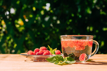Drink from ripe red raspberries in a transparent mug, a plate with a berry, a summer background. Summer seasonal drinks