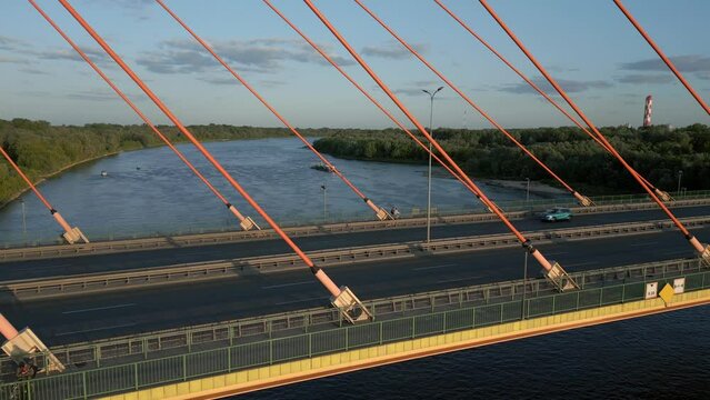 Aerial perspective, capturing a parallel flight along the pylon bridge at sunset, showcasing cars and cyclists in motion