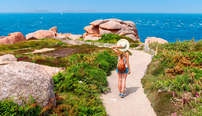 Woman tourist walking on footpath, pink granite coast in Brittany- France