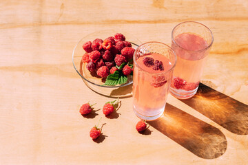 Ripe red raspberry drink in a transparent glass wooden background, summer seasonal food and refreshing drinks