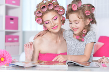 Obraz na płótnie Canvas Mom and daughter with hair curlers reading magazine