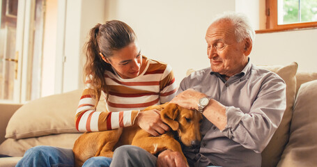 Portrait of a Senior Man and his Daughter Petting the Family Dog Laying on their Lap. They are...