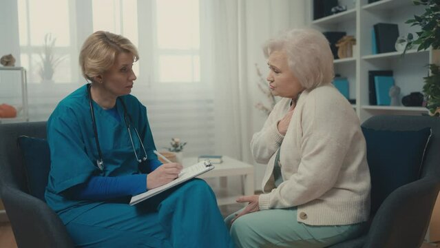 Therapist talking to sick senior patient, filling in medical records, home visit