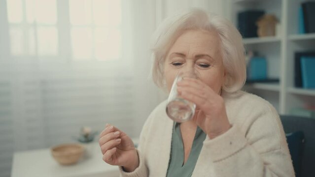 Senior lady taking pill, drinking glass of water, disease treatment medication