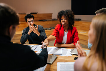 Rear view of Caucasian businessman handshaking with African businesswoman after signing contract, members of meeting clapping hands, to celebrating of achieving goals success in meeting room.