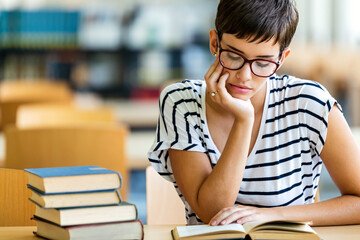 Exhausted young female studying and preparing for exam in college library. Education people concept