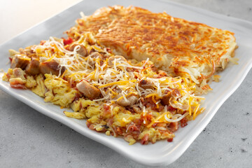 A view of a breakfast plate featuring bacon, sausage, scrambled eggs, and hash browns.