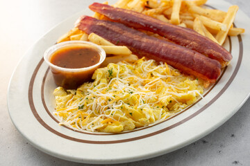 A view of a breakfast plate, featuring turkey bacon, scrambled eggs, shredded cheese and french fries.