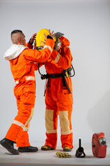 Professional firefighter is helping his partner wearing a yellow hard hat on a white background.