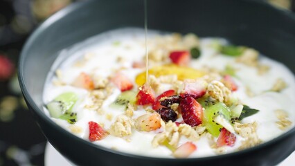 Honey pouring on fruit berry salad with yogurt and granola for healthy breakfast. Honey, yogurt and fresh berries in bowl. Healthy food concept