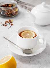 Tea with lemon in a white cup on a light background with  a teapot. The concept of a healthy and tasty breakfast for immunity