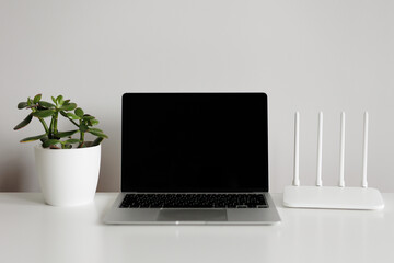 Laptop, router and green plant on white table