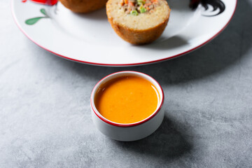 A view of a condiment cup of an orange colored Indonesian peanut dipping sauce.