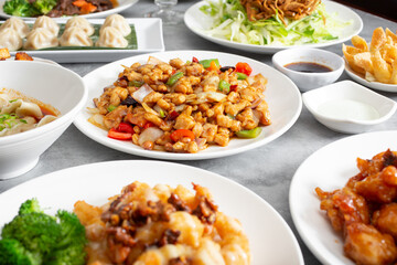 A view of a table full of various Chinese entrees, featuring kung pao chicken.