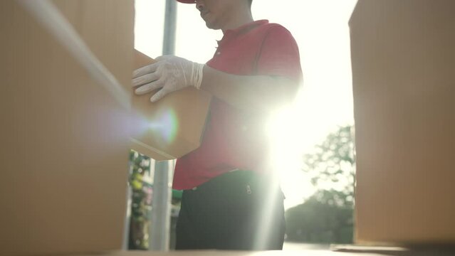 A parcel delivery worker dressed in a red uniform is lifting a package from the trunk of the truck to the recipient. contact the receiver in front of the house.