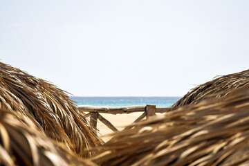 Beach umbrella made from dry palm leaves. Summer travel and vacation concept. Texture of dried leaves. Roof of sun parasol is made of dried palm branches. Copy space. Selective focus.
