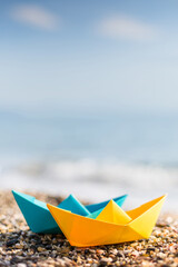 Blue and yellow paper boats on the pebble beach