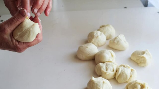 Close-up of wrinkled hands of an elderly woman pinching off raw dough to form balls. An old grandmother bakes buns using a traditional family recipe.