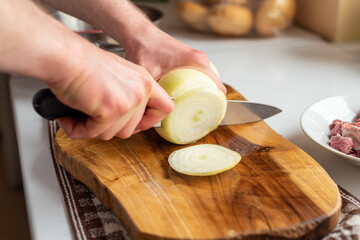 A man cuts onions on a wooden board with a sharp knife