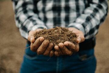 Oldman farmer holding soil in cupped hands.