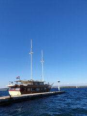 Fototapeta na wymiar two mast wooden ship with Croatian flag moored in dock against clear blue sky with space for text