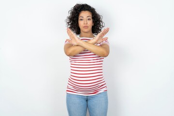 young pregnant woman wearing striped t-shirt over white background has rejection expression crossing arms and palms doing negative sign, angry face.