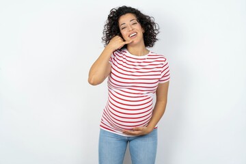 young pregnant woman wearing striped t-shirt over white background smiling doing phone gesture with hand and fingers like talking on the telephone. Communicating concepts.