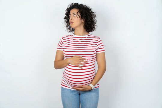 Close up side profile photo young pregnant woman wearing striped t-shirt over white background not smiling attentive listen concentrated