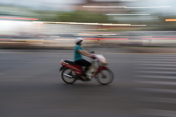 Obraz na płótnie Canvas Person on scooter motorbike speeding through the city street - motion blur shot 