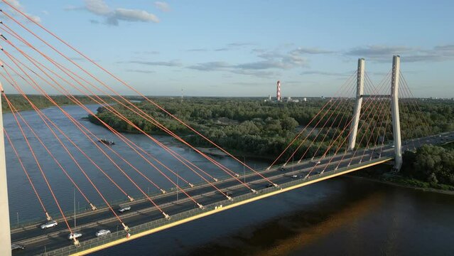 Aerial flyover between sunset-lit pylons of Siekierkowski Bridge, overlooking distant coal power plant in Warsaw