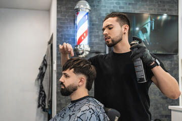 Barber combing his client's hair with his fingertips and fixing his hair with hairspray.