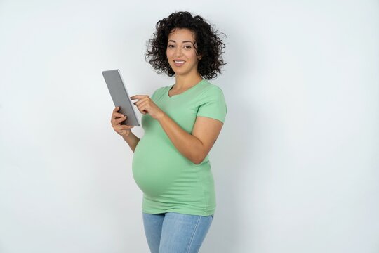 Photo of happy cheerful smart young pregnant woman wearing green t-shirt over white background hold tablet browsing internet