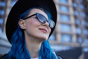 Cheerful diverse woman with dyed blue hair. Portrait of a beautiful female person wearing stylish hipster hat and sunglasses outdoor. Beauty and diversity concept