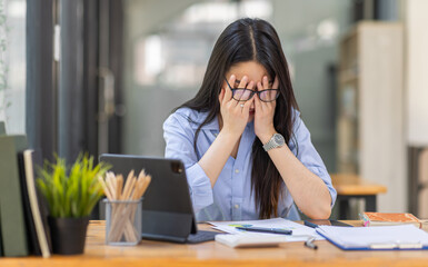 Portrait of tired young business Asian woman work with documents tax laptop computer in office. Sad, unhappy, Worried, Depression, or employee life stress concept
