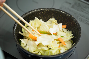 野菜炒めを作る若い女性　料理イメージ